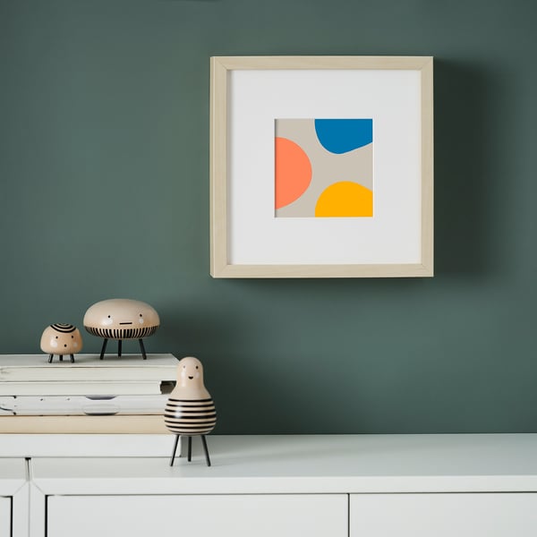 Abstract art on green wall with blue, orange, yellow shapes. Below, white shelf with wooden figures and books.