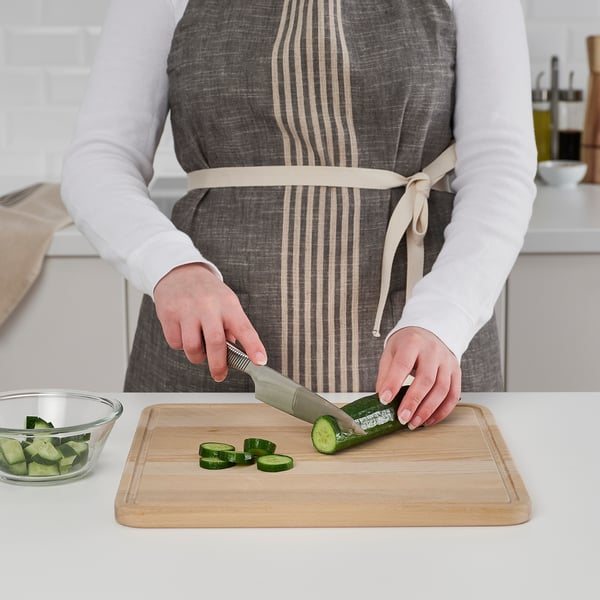 Person slicing cucumber on reversible wooden chopping board with juice groove.