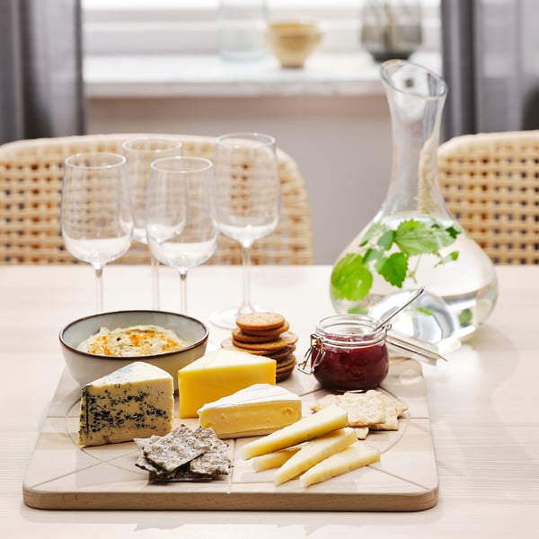 Wooden chopping board with various cheeses, crackers, and empty wine glasses on a table. Ideal for serving and preparing food.