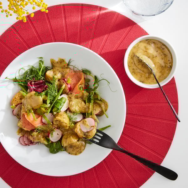 Bright salad with mustard sauce on white plate, black fork, red placemat.