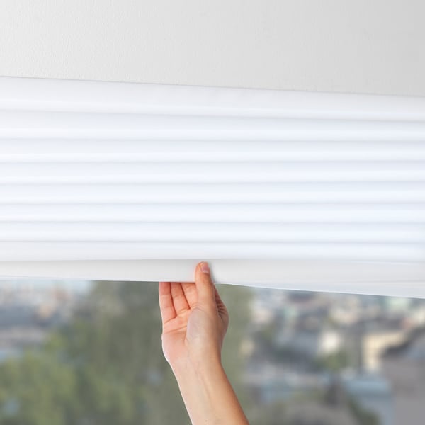 A hand adjusting a white, pleated privacy screen, blocking glare and offering slight privacy.