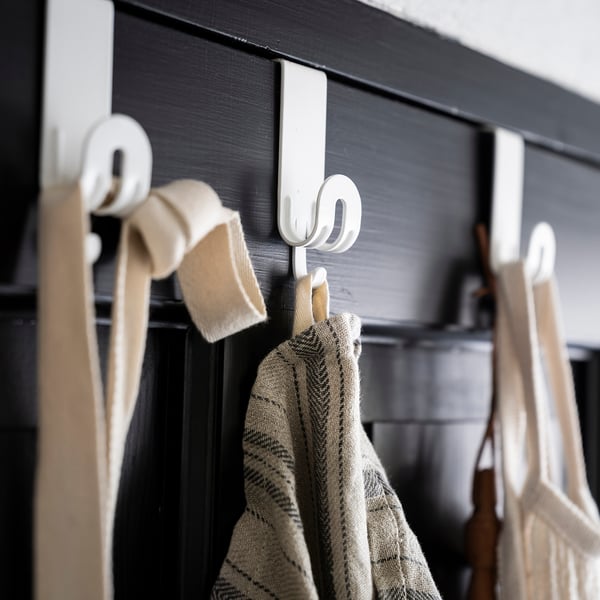 White metal hooks hang on a dark wooden surface, holding light-colored towels.