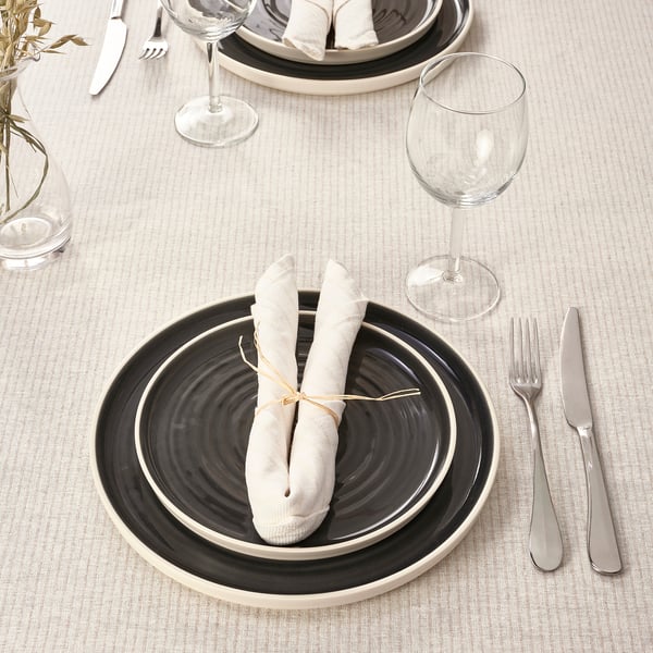 Table set with black and white plates, rolled napkins, silverware, and wine glasses on a beige tablecloth.