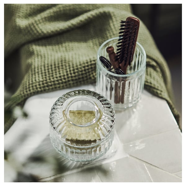 Clear glass bathroom accessories: jar and toothbrush holder with intricate design.