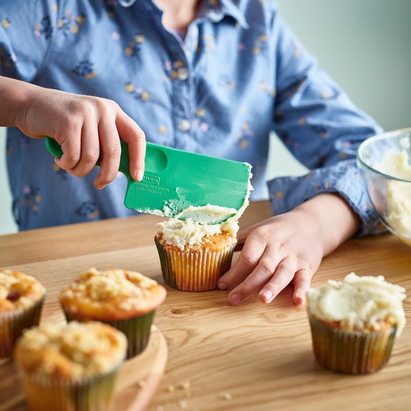 A person using green SJÖRUDA spatula to frost cupcakes with precision.