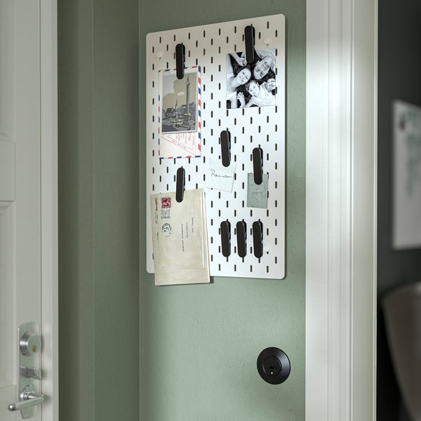 A pegboard, SKÅDIS, hangs on a green wall, displaying photos, notes, and envelopes, providing organised display and easy access.