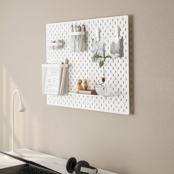 Wall-mounted white pegboard with organisers, books, vase, and notes. Home office storage.