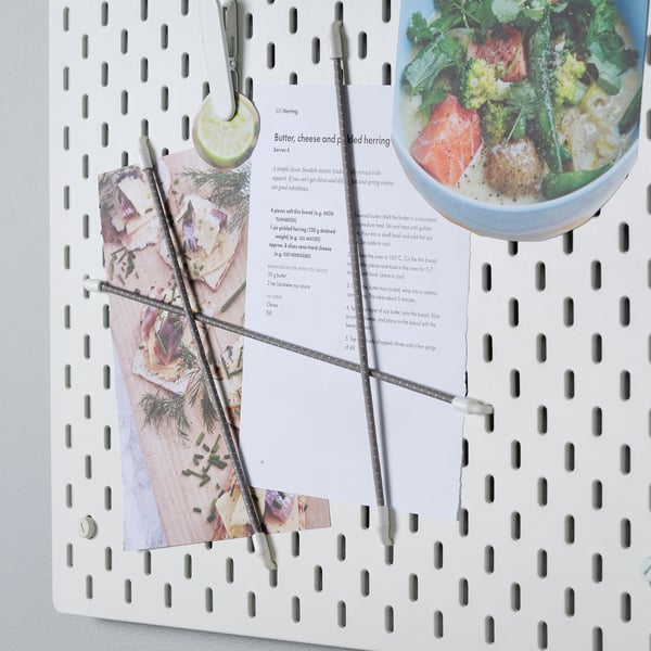 White pegboard with hydrogen clips holding recipes and utensils.