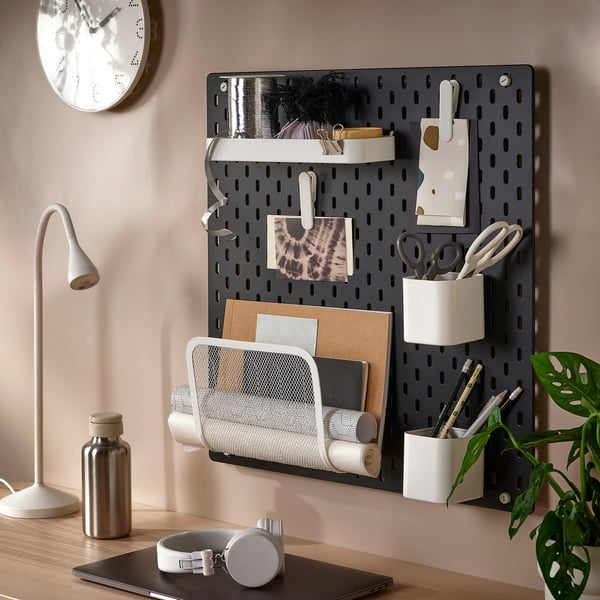 Wall-mounted SKÅDIS pegboard organises office supplies, holding scissors, pens, paper rolls, and notes in a stylish and functional setup.