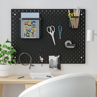 SKÅDIS black pegboard organising office supplies, photos & accessories above desk.
