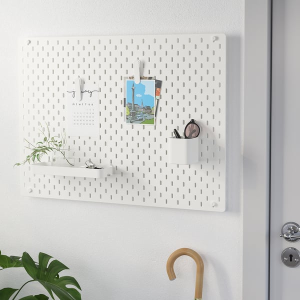 White SKÅDIS pegboard with hooks, cup, plant, calendar, and photo holds various items neatly. Ideal for organizing entryways or offices.