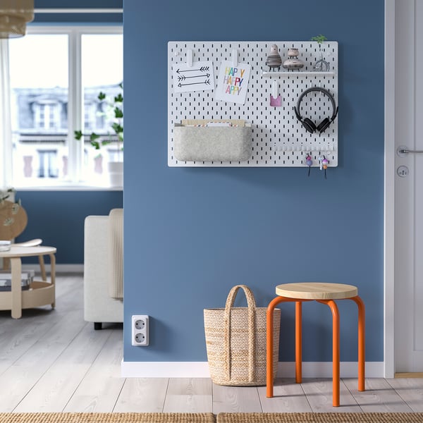 Blue wall with white SKÅDIS pegboard and orange stool holding a white basket.