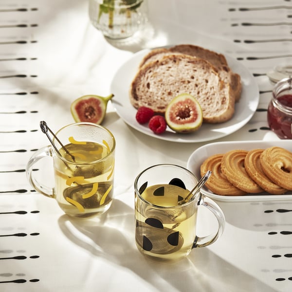 Table setting with two teacups, bread, pastries, and fruits. Teacup handles show secure grip.