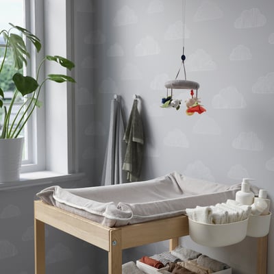 Nursery with cloud wallpaper, changing table, mobile, plant, towels.