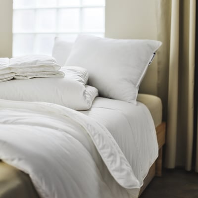 Large, neatly-made bed with white SKOGSFRÄKEN duvet & pillows, soft & fluffy, bright lighting.