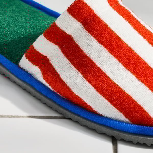Bright striped slippers with non-slip sole, featuring orange and white stripes, blue trim, and green interior on a grey tiled floor.