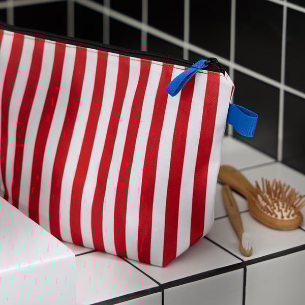 Red and white striped travel bag with blue zip sits on tiled surface beside wooden brush and toothbrush. Easy to organise and clean.