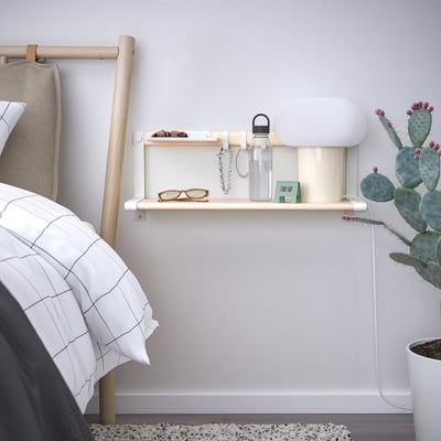 Light wood wall shelf with hooks, holding water bottle, glasses, and jewellery near bed.