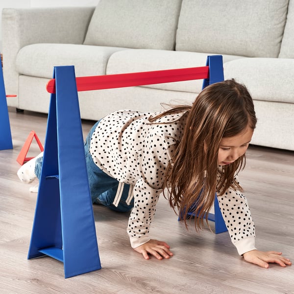 A child crawling under a blue and red obstacle course set in a living room.