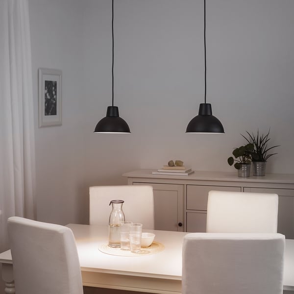 Black SKURUP lamps hang above a dining table with white chairs.