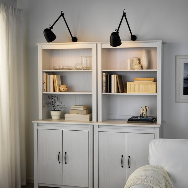 White wall unit with black adjustable lamps, holding books. Fills most of the wall.