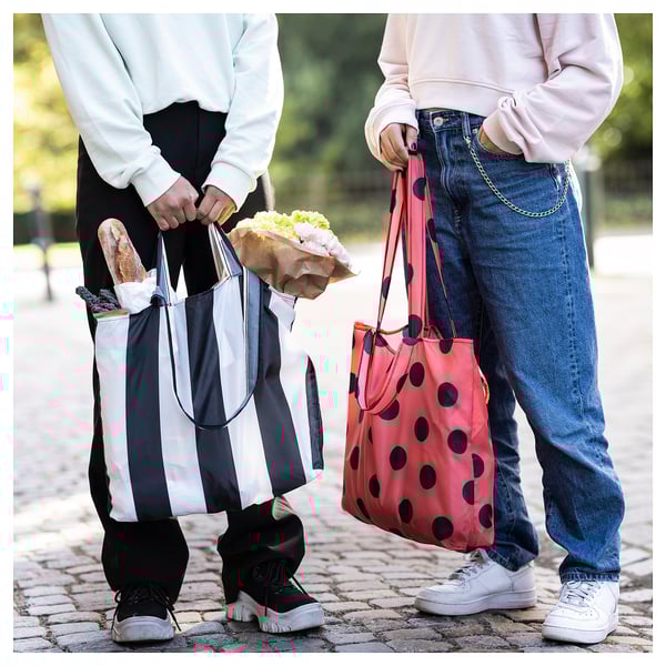 Two people holding shopping bags; one black & white striped, one red with black spots.