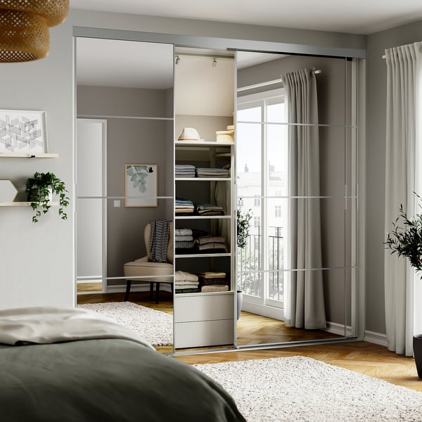 Modern bedroom with mirrored closet doors, green headboard bed, and large windows with grey curtains.