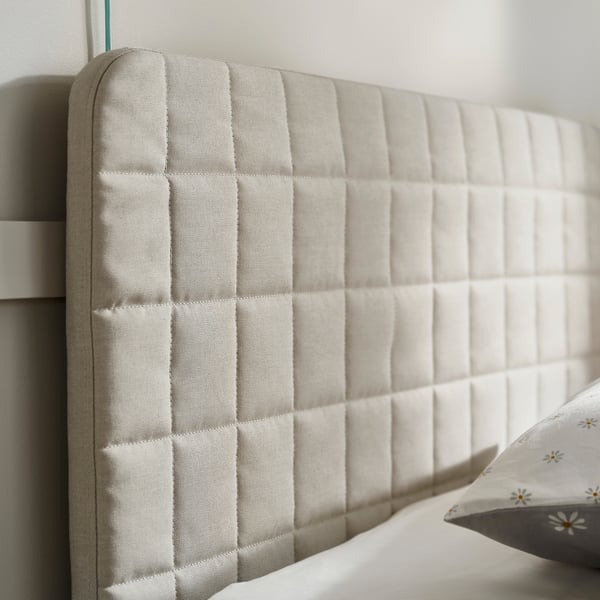 Soft, quilted beige bed headboard with diamond pattern, mounted against white wall. Comfortable and stylish bed design.
