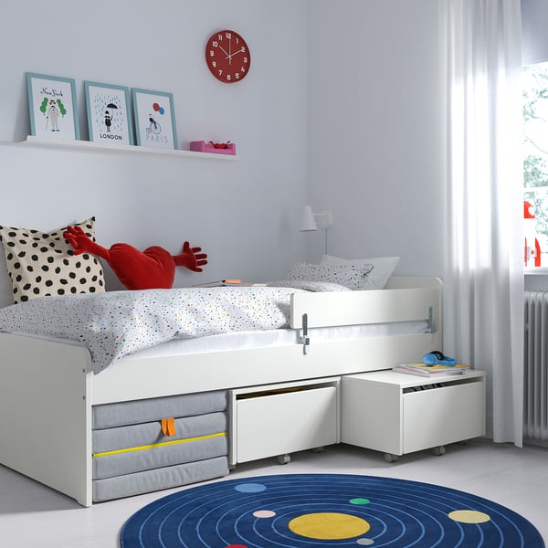 Kids room with white SLÄKT bed, storage, & decor. Bright red clock, city prints, playful rug.