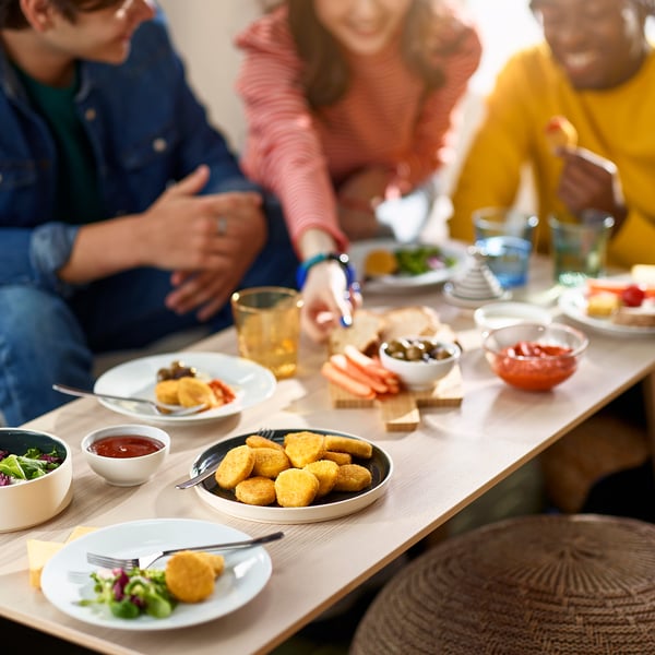People enjoying a meal at a table with plates of breaded wheat-based pieces, salad, and dipping sauces.