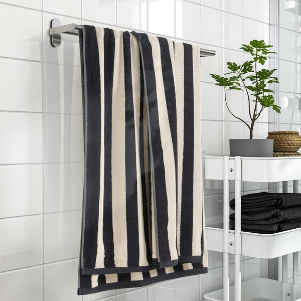 Black & white striped SLÅNHÖSTMAL towel on rack, dark towels, plant on shelf.
