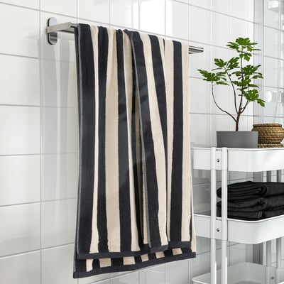 Black & white striped SLÅNHÖSTMAL towel on rack, dark towels, plant on shelf.