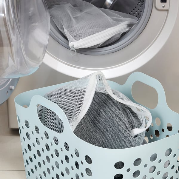 Washing machine with light blue laundry basket holding mesh bag full of knitted sweater for gentle washing.