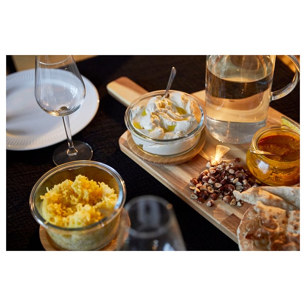 Wooden charcuterie board with cheese, hazelnuts, jam, and glassware. Ideal for serving and knives.