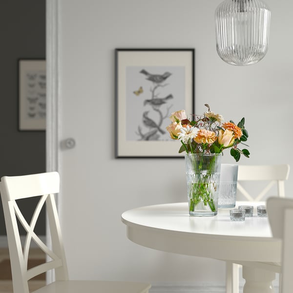 Bright dining room with SMÄLLSPIREA clear vases on small white table, holding orange flowers, next to white chairs.