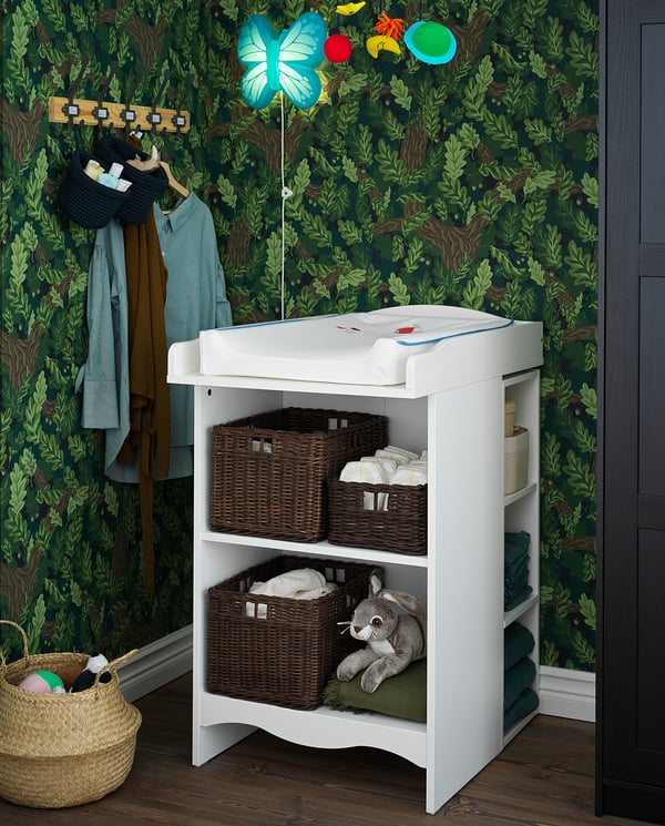 Childs changing table with wicker baskets. Bright nursery decor with green walls.