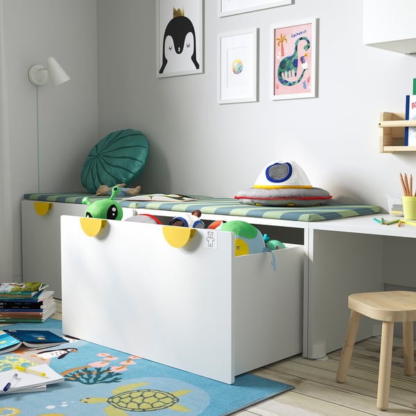 Childs room with white storage bench for toys, colourful pillows, and wall art.