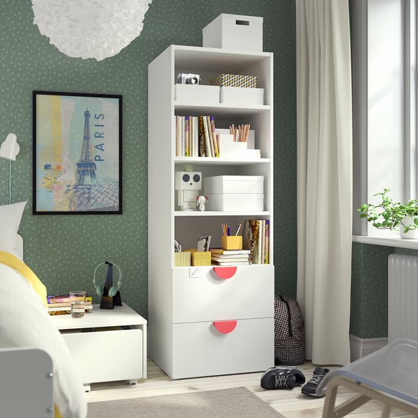 White bookcase in bedroom with books, decor, and paris poster. Green patterned walls, window with curtains.