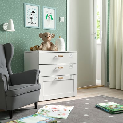 Cosy nursery with SMÅSTAD chest, grey chair, bear toy, city art, open book.