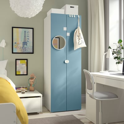 Blue SMÅSTAD wardrobe towers near white desk and chair. Room includes bed with yellow pillows, art, rug.
