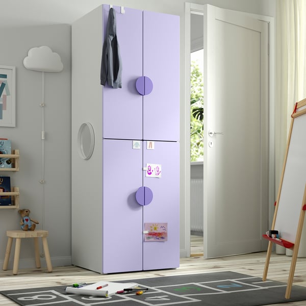 A tall, light purple SMÅSTAD wardrobe for a kid’s room with two doors, circular handles, and a clothes rail on top, standing near a door.