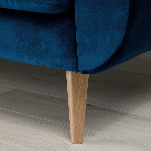 Blue velvet sofa with tapered wood legs under low light.