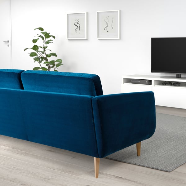 Modern living room with blue velvet sofa, tv, art, plant.