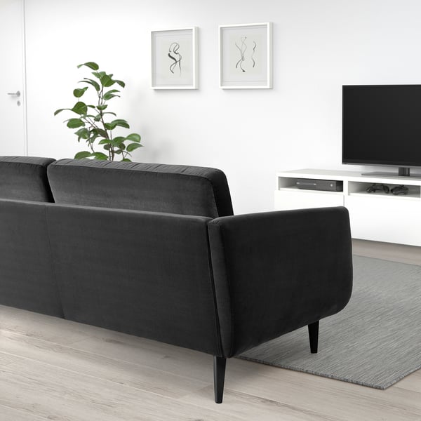 Modern living room with black velvet SMEDSTORP sofa, cushioned armrests, and high legs. Tv on white stand, plant on floor, minimalist decor.