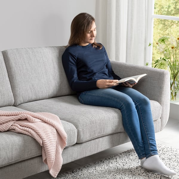 Woman reads book on cozy sofa with armrests, textured fabric & cone legs.