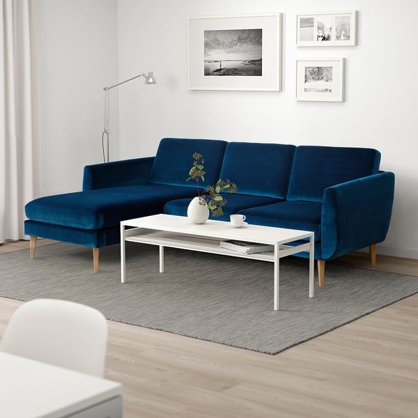 Modern living room with large blue velvet SMEDSTORP sofa, white coffee table, grey rug, and wall art. Bright and inviting.