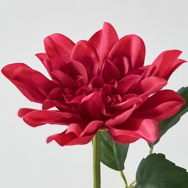 Bright crimson artificial dahlia with lush green stem and leaves, vividly coloured, detailed folds.