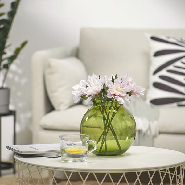 Small green vase with pink flowers on round coffee table with lemon cup and magazine.