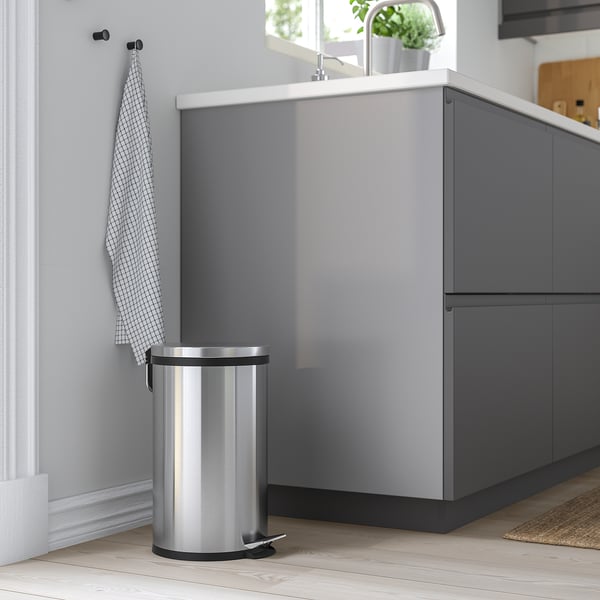 Silver pedal bin in modern kitchen with grey cabinet and white wall. Easy to move with handle.