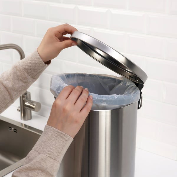 Person placing a plastic bag inside a stainless-steel pedal bin with a handle, suitable for waste or recycling in the kitchen or bathroom.